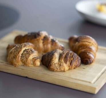 Vier frisch gebackene Croissants auf einem Holzbrett – Frühstücksangebot im MeetingRAUM Ingolstadt.