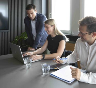 Drei Personen arbeiten gemeinsam an einem Laptop bei einem Meeting im modernen Besprechungsraum des MeetingRAUM Ingolstadt.