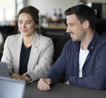 Zwei beruflich gekleidete Personen sitzen nebeneinander an einem Tisch und schauen gemeinsam auf einen Laptop – Meeting oder Zusammenarbeit im MeetingRAUM Ingolstadt.