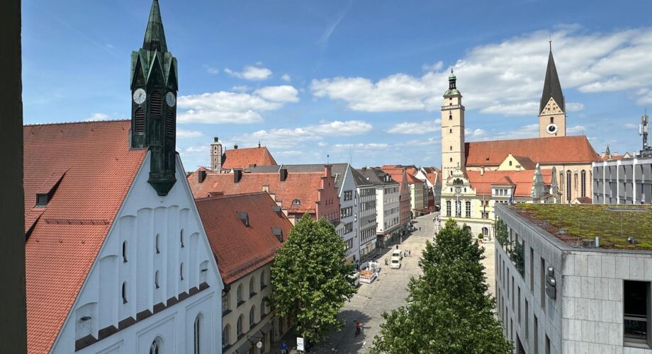 Panoramablick über die historische Altstadt von Ingolstadt mit roten Dächern, Kirchen, Rathaus und barocken Gebäuden unter blauem Himmel, aufgenommen vom MeetingRAUM aus.