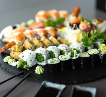 Sushi-Auswahl auf einer runden Schieferplatte, Wasabi, Crunchy Sushi, vegetarisches Sushi, Nigiri, Maki mit bunter Deko – serviert im MeetingRAUM Ingolstadt.